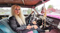 Nainen istuu autossa kuljettajan paikalla ja katsoo kohti kameraa