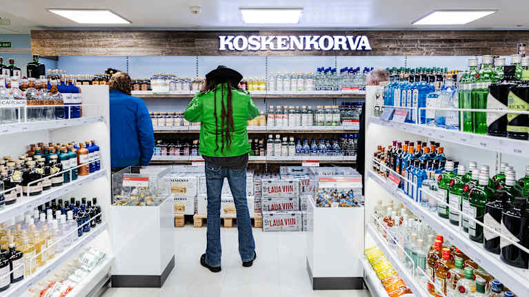 Matkustajia Koskenkorva-hyllyn edessä.