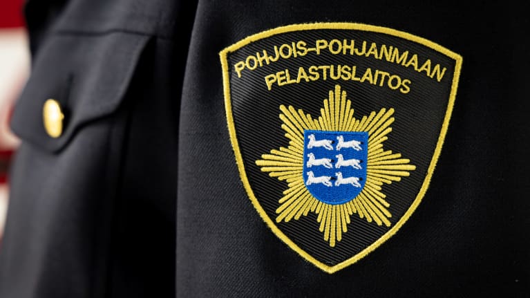 Pohjois-Pohjanmaan pelastuslaitoksen logo hihassa ja palo-autojen kyljessä.