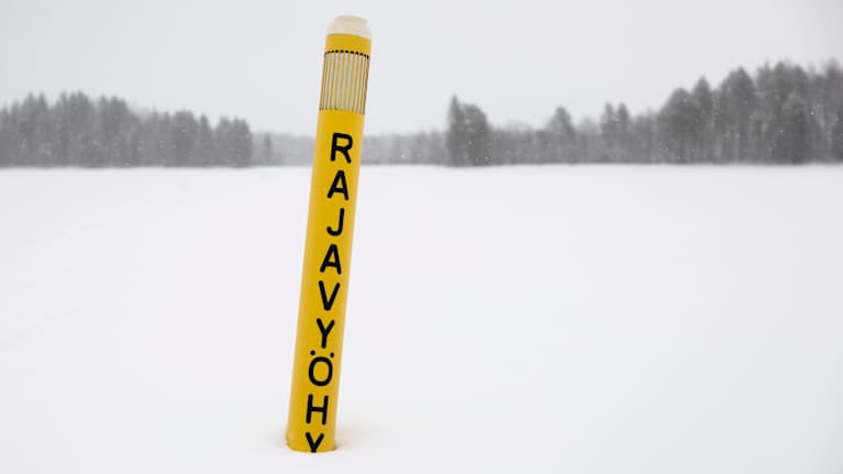 Rajavyöhykkeen tolppa hangessa järven jäällä.