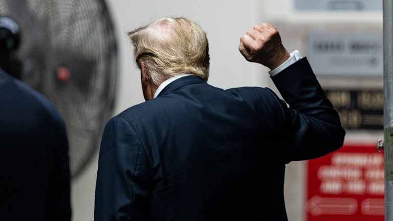 Donald Trumpin selkäpuoli. Hän nostaa nyrkkiin puristettua kättään ylös tervehdykseen.