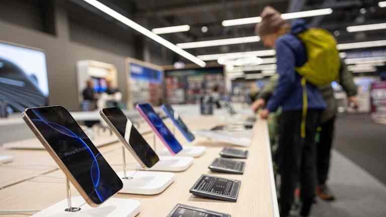 Iphone-puhelimia esillä myymälässä, taustalla asiakkaita.