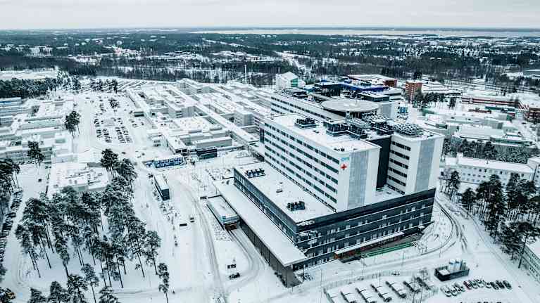 Kuvassa on talvinen maisema, jossa näkyy suuri sairaalarakennus lumisessa ympäristössä. Rakennus on OYS, eli Oulun yliopistollinen sairaala, joka sijaitsee Oulussa, Suomessa. Uusi rakennus kuvan edessä, takan vanha sairaala joka puretaan.