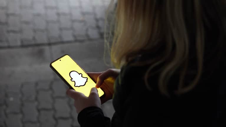 Henkilö käyttää Snapchat-sovellusta älypuhelimellaan ulkona hämärässä valaistuksessa.