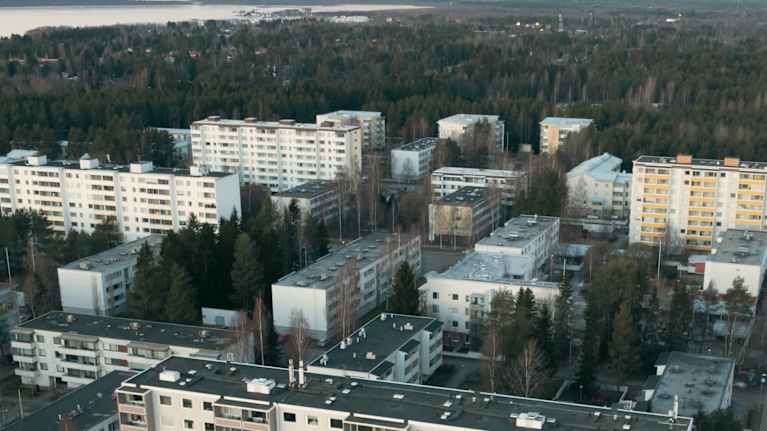 Ilmakuva suomalaisesta lähiöstä, jossa näkyy useita kerrostaloja sekä taustalla metsää ja vesistöä.