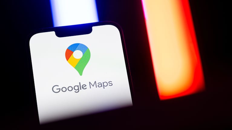 Puhelimen näytöllä näkyy Google Maps -sovelluksen logo, taustalla punaisia ja sinisiä valoja.