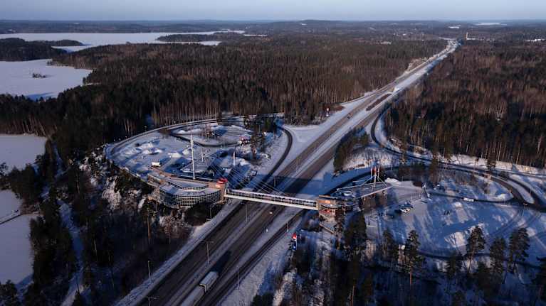 Valtatie ja iso liikenneasema liittyminen ilmakuvassa. Talvinen järvimaisema taustalla.