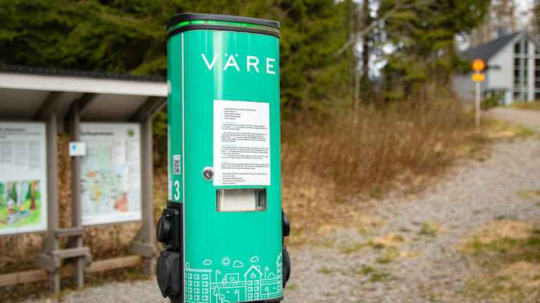 Vihreän värinen sähköauton lataustolppa, jossa teksti "Väre".