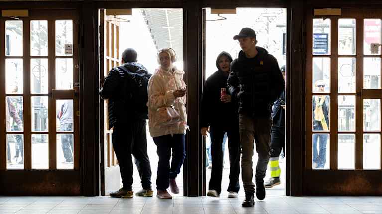 Ihmisiä astumassa sisään rakennukseen kirkkaasta päivänvalosta.