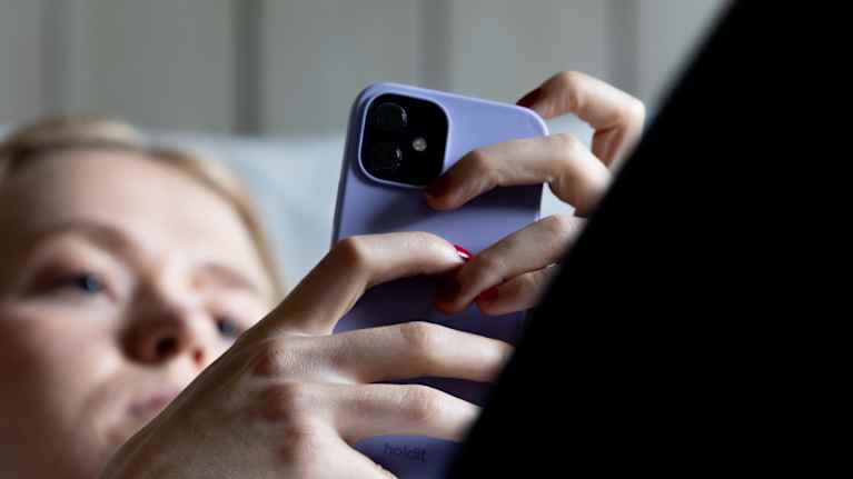 Henkilö tutkii puhelintaan sängyllä maaten.