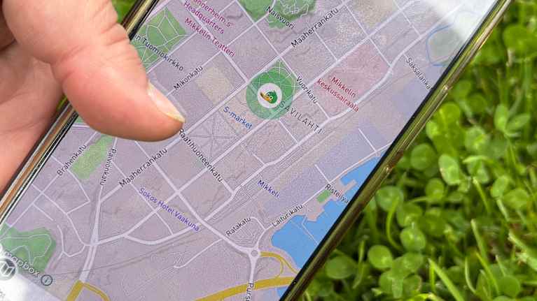 Käsi pitää kännykkää, jonka näytössä näkyy karttasovellus.