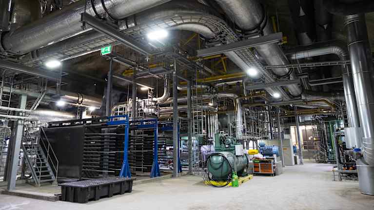 Maanalainen teollisuushalli, jossa paljon laitteita ja eristettyjä putkia.