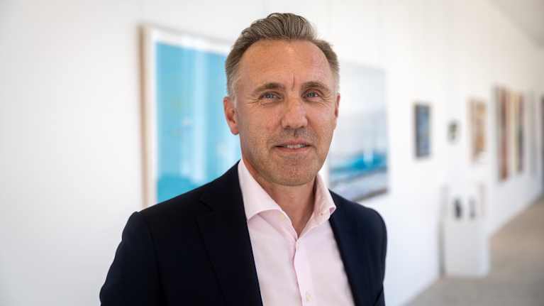 Analyytikko Kimmo Stenvall puolilähikuvassa kuvattuna valoisassa aulassa. Taustalla näkyy maalauksia vaalealla seinällä.