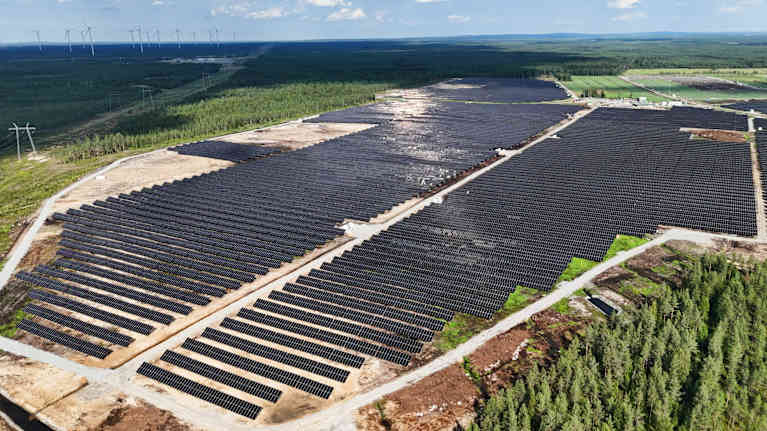 Aurinkovoimala jossa tuhansia aurinkopaneeleita. Taustalla näkyy myös tuulivoimaloita.