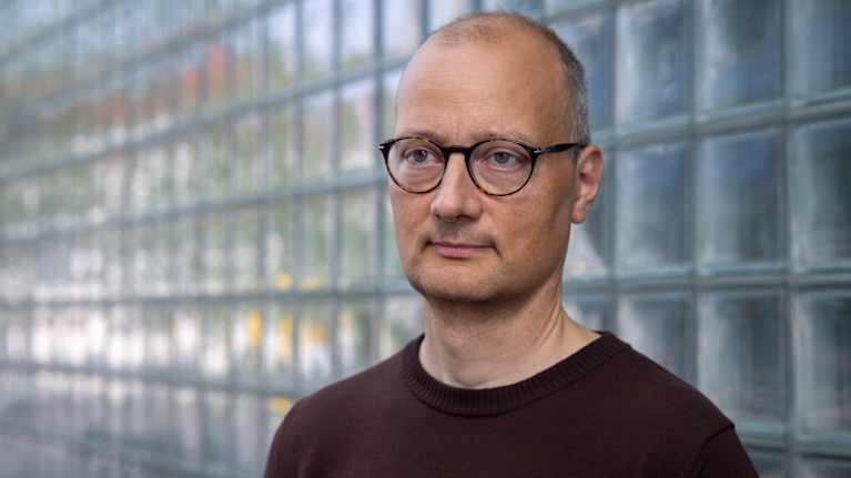 Niku Määttänen seisoo lasitiiliseinän edessä.