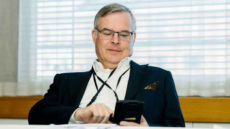 Henkilö istuu pöydän ääressä ja käyttää puhelinta