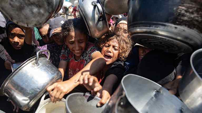Lapset ojentavat kattiloita saadaseen ruoka-apua avustuspistee.