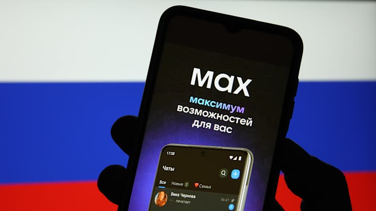 Käsi pitelee älypuhelinta Venäjän lipun väristä taustaa vasten. Näytöllä lukee Max ja venäjäksi: maksimaaliset mahdollisuudet teille.
