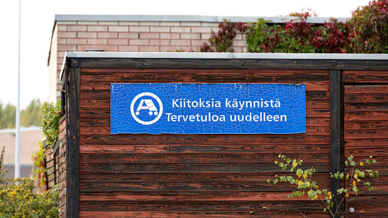 Sininen Ajovarman kyltti puisella seinällä, jossa lukee "Kiitoksia käynnistä Tervetuloa uudelleen".