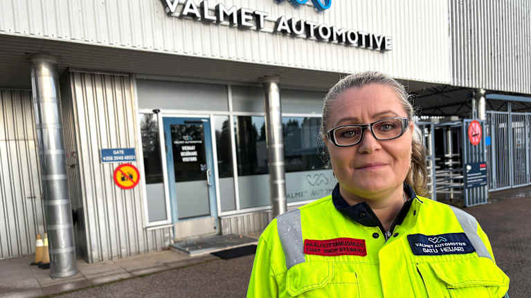 Keltaiseen turvaliiviin pukeutunut silmälasipäinen nainen, taustalla kyltti Valmet Automotive.