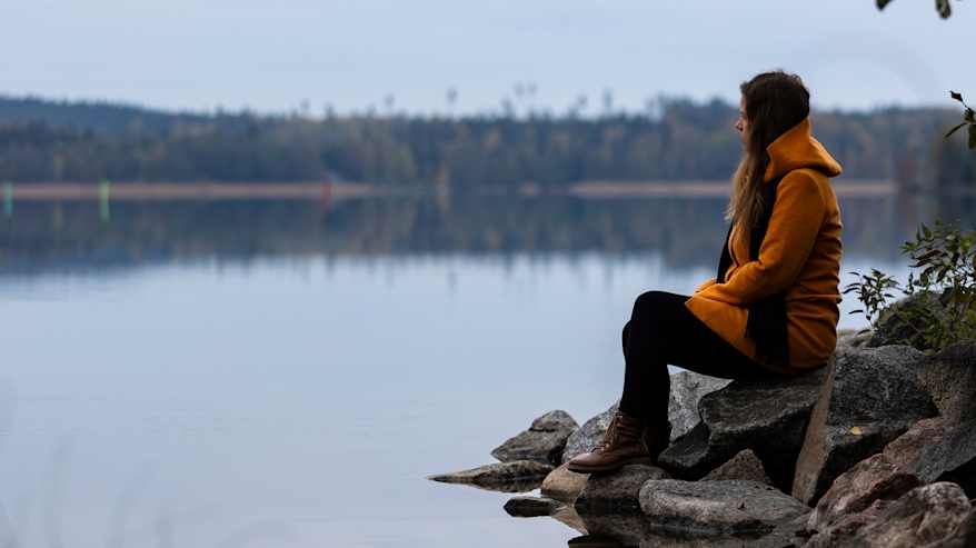 Nainen istuu rantakivillä.