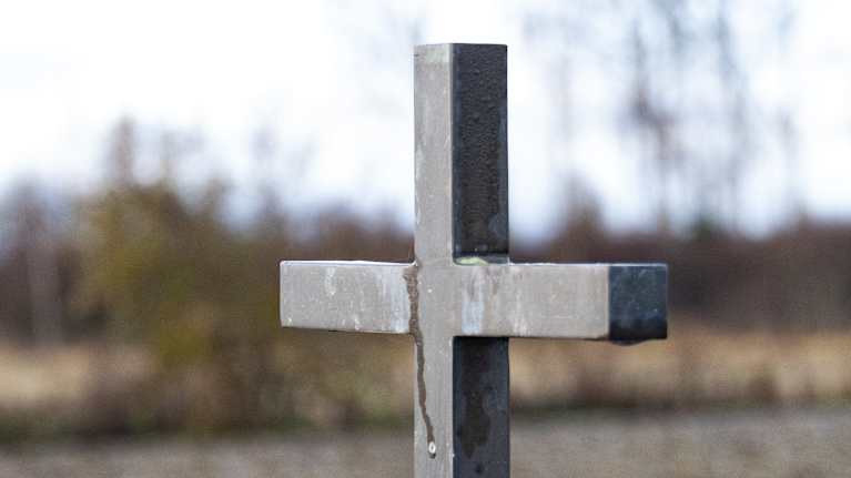 Vanha hautaristi seisoo pellolla olevalla hautamuistomerkillä.