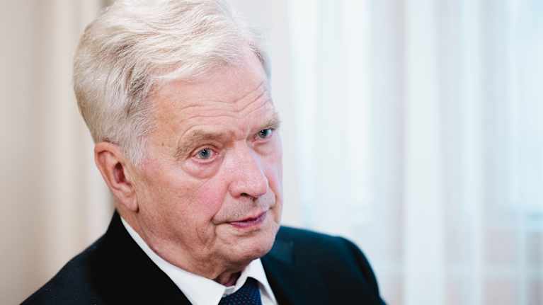 Sauli Niinistö istuu vaaleiden verhojen edessä