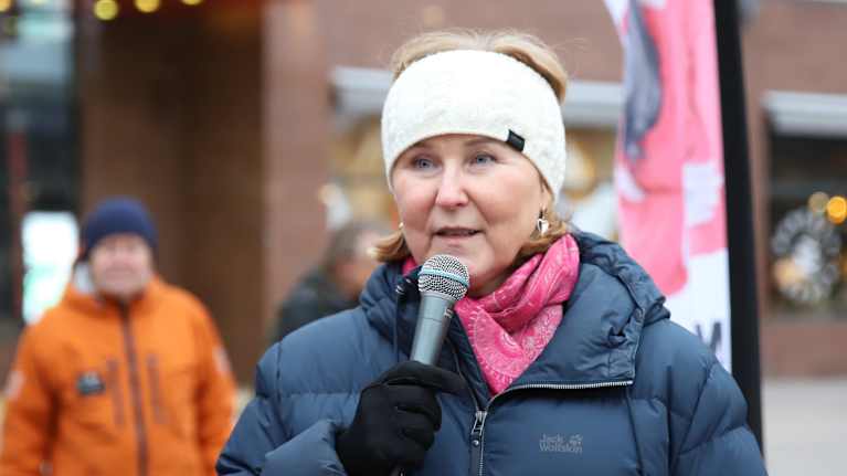 Kaisa Juuso tummansinisessä toppatakissa puhuu mikrofoniin ulkona.