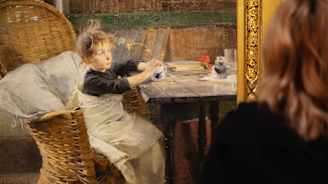 Helene Schjerfbeckin maalaus Toipilas. Lapsi tarkastelee hiirenkorvalle puhkeavaa oksaa, istuu korituolissa pöydän ääressä.YleGPT:n generoima ehdotus kuvailevasta tekstistä:  Kuvassa nainen katsoo taidemaalari Albert Edelfeltin teosta "Leikkiviä poikasia rannalla". Maalauksessa nuori poika istuu korituolissa pöydän ääressä ulkona ja leikkii. Tämä teos on esillä taidemuseossa, ja siitä voi nauttia osana suomalaisen taiteen ja kulttuuriperinnön näyttelyä.