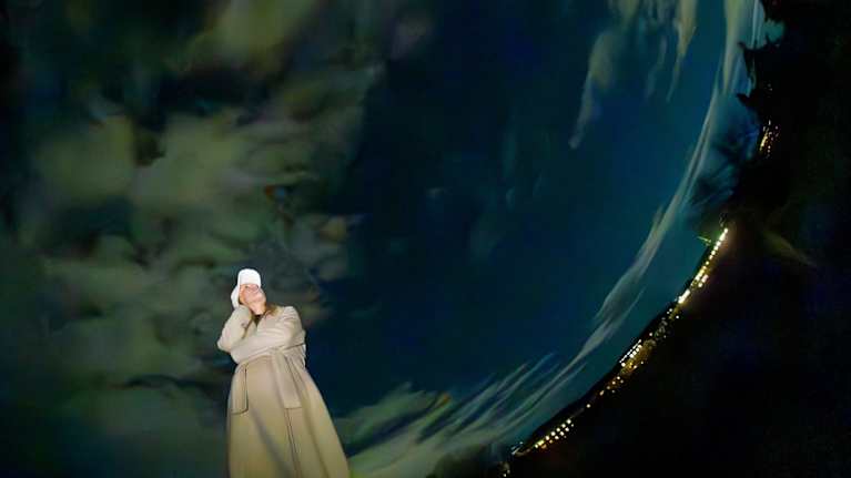 Nainen kaupungin maisemassa yöllä, pilvinen taivas kaartuu kuin maapallon muotoon.