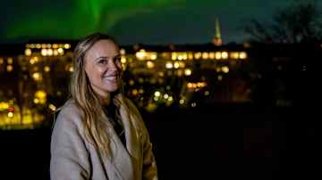 Nainen nauttii upeasta revontulien näytelmästä kaupungin yllä.