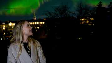 Nainen nauttii upeasta revontulien näytelmästä kaupungin yllä.