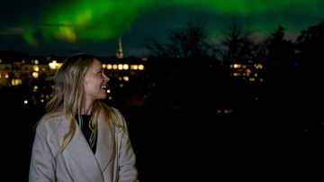 Nainen nauttii upeasta revontulien näytelmästä kaupungin yllä.