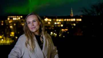 Nainen nauttii upeasta revontulien näytelmästä kaupungin yllä.