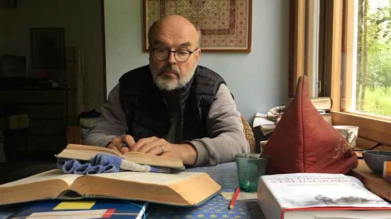 Kirjailija ja suomentaja Martti Anhava lukee pöydän ääressä kirjaa.