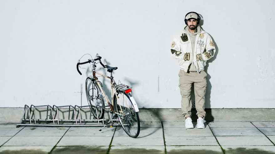 henkilö seisoo ulkona kuunnellen musiikkia kuulokkeista, vieressään parkkeerattu polkupyörä telineessä.