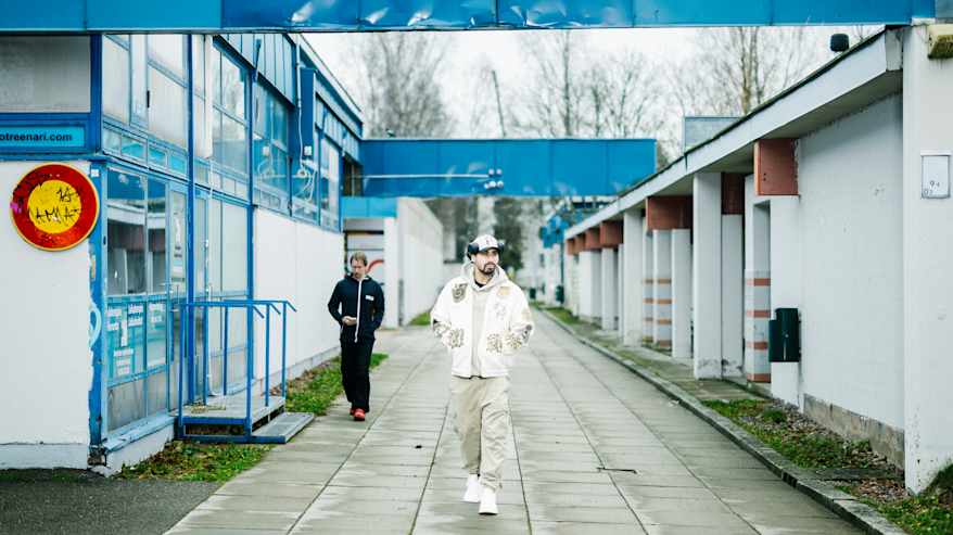 Mies kävelee kauppakeskuksen edustalla pukeutuneena vaaleaan asuun.