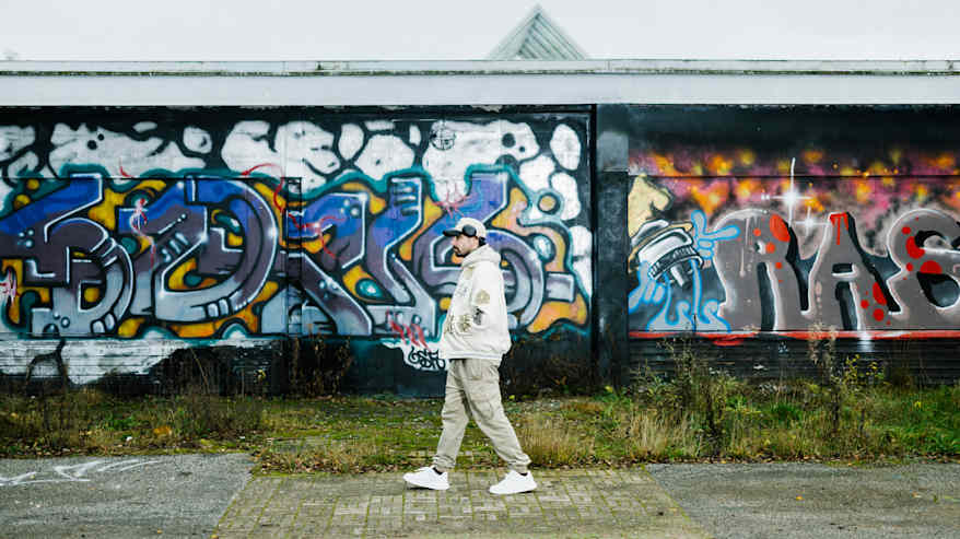 Henkilö kävelee värikkäiden graffitien peittämän seinän edessä.