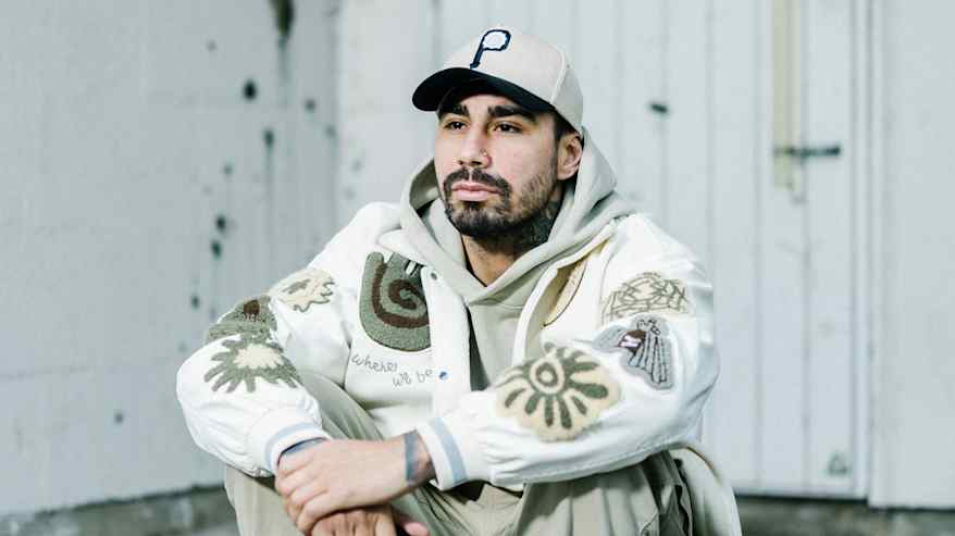 Henkilö istuu portaalla. Hänellä on lippalakki päässä ja kuulokkeet kädessä.