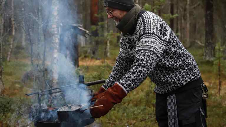 Mies keittää kahvia metsässä avotulella.