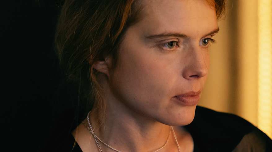 Alina Tomnikov kuvattuna lämminsävyisessä valossa ja ympäristössä. Ilme on neutraali ja Alina katsoo sivuun..