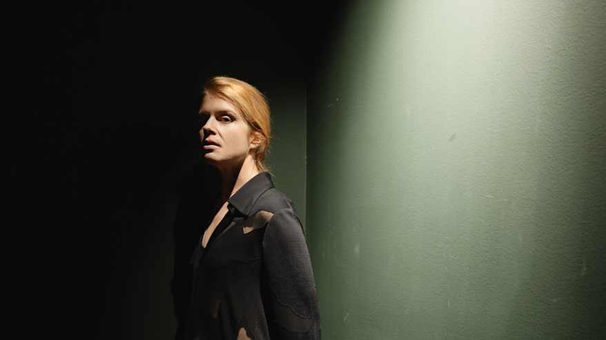 Alina nojaa seinään tummassa rappukäytävässä, ylhäältä osuu häneen dramaattinen valo.