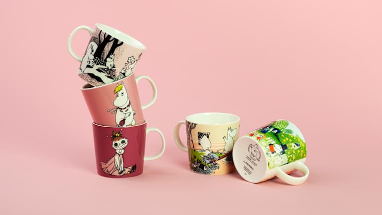 Viisi muumimukia on esillä vaaleanpunaista taustaa vasten.