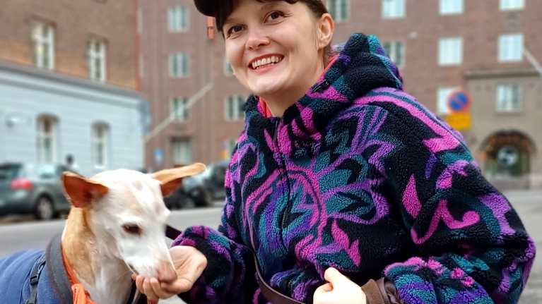 Iiti Yli-Harja hymyilee Rontti-koiran kanssa syksyisessä kaupunkimaisemassa. 