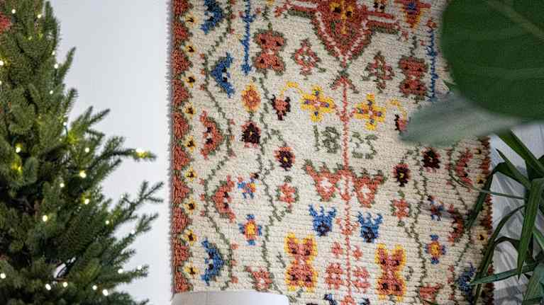 Kuvassa on värikäs ryijy, jossa näkyy perinteisiä kukka- ja geometrisia kuvioita. 