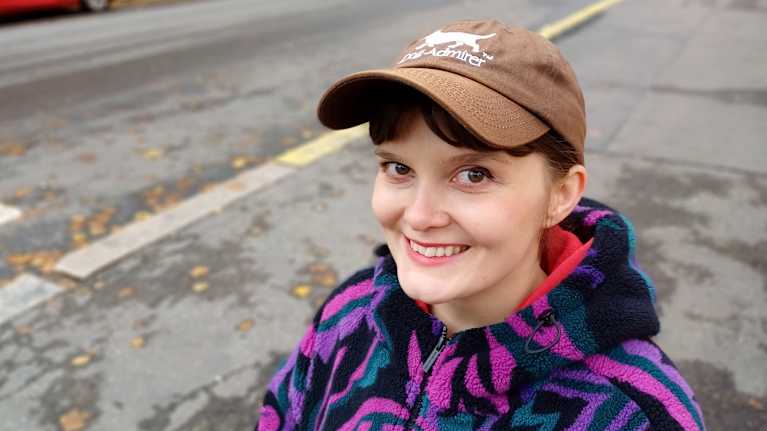 Iiti Yli-Harja hymyilee Rontti-koiran kanssa syksyisessä kaupunkimaisemassa. 