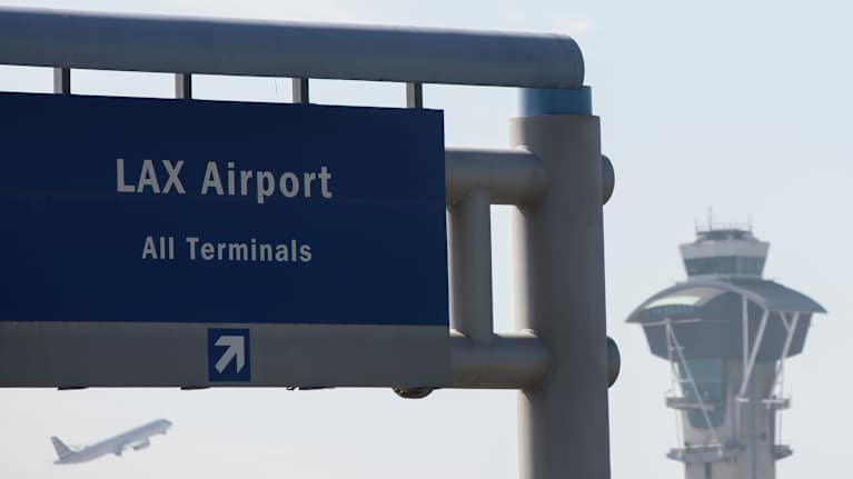 Ett flygledartorn och en skylt som visar att vi är på Los Angeles flygplats. Ett flygplan lyfter i bakgrunden.
