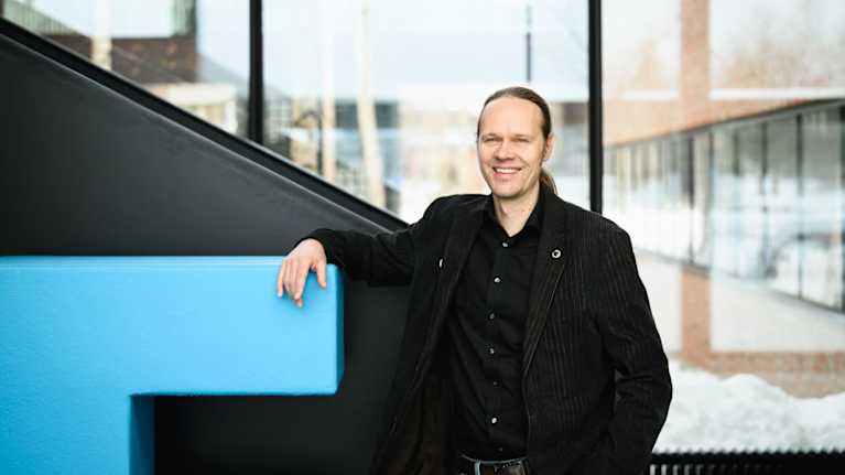 Itä-Suomen yliopiston professori Jaakko Pohjoismäki hymyilee ja katsoo kameraan, taustalla yliopiston tilojen lasiseinä ja portaikko.