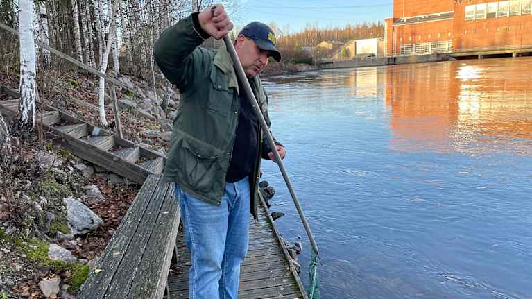 Mies seisoo laiturilla ja näyttää saaneensa jotakin merestä haaviinsa. Taustalla näkyy teollisuusrakennus.