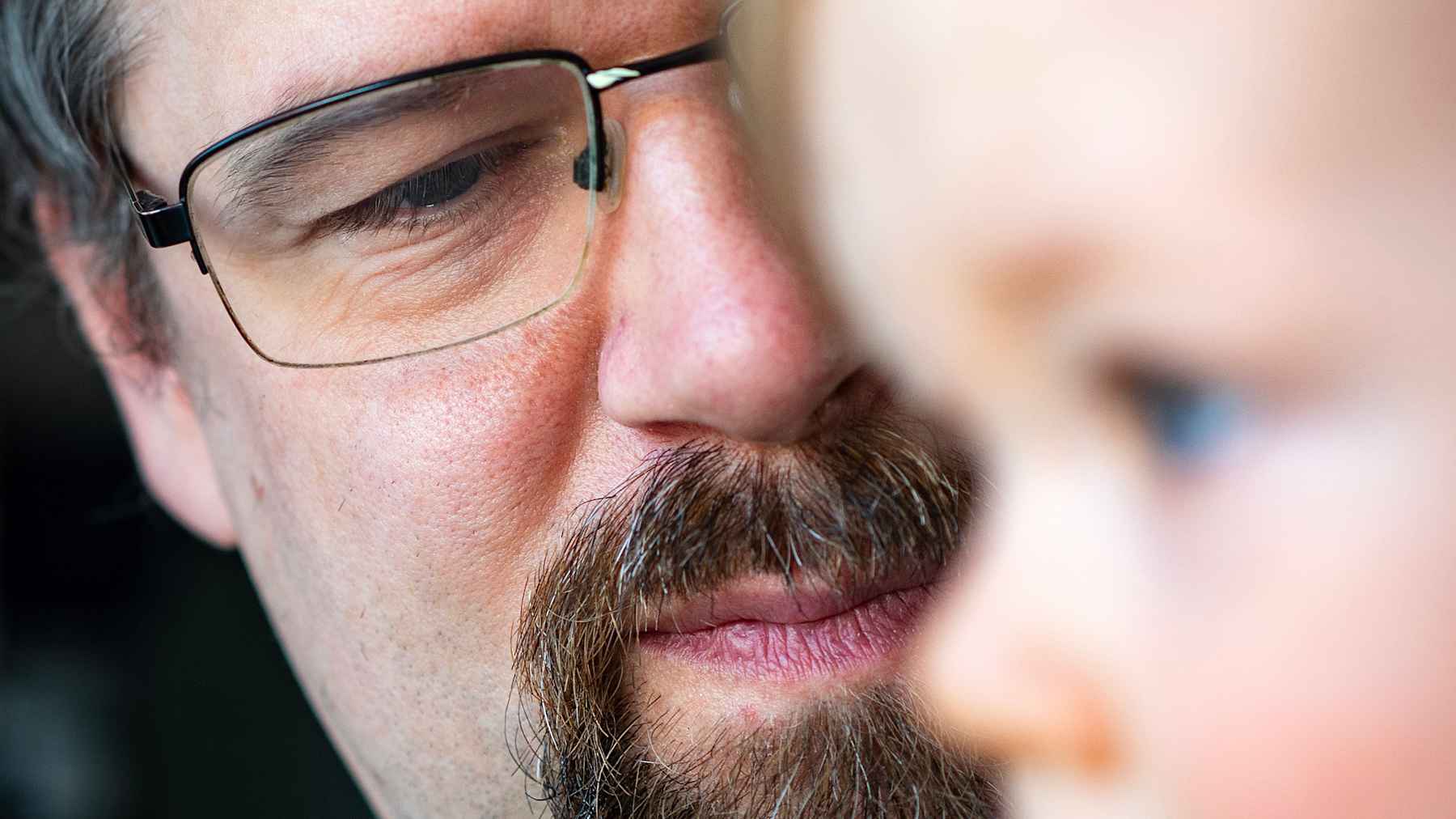 Paiste Mäenpää pitää lasta sylissään. Lapsi on etualalla epäterävänä ja pitää kädessään värikästä, vihreää lelua.